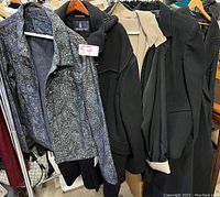 Group of womens jackets and coats in a rack, showing different styles and brands including a silver textured jacket