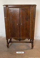 Front view of antique wooden cabinet with two doors and carved decorative elements on legs and front panel.