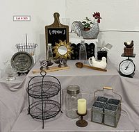 Full overview of the kitchen and decorative items arranged on draped fabric showing the entire lot of items including containers, bottles, metal and wooden decor, and tools.