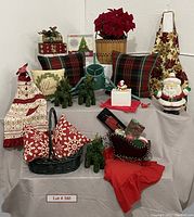 Full lot view showing pillows, reindeer, Santa bank, aprons, basket, and other items arranged on cloth-covered table.
