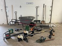Full lot view showing wheelbarrow, shovels, rakes, blowers, trimmers, and smaller tools arranged on floor.