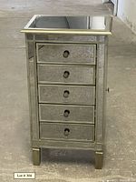Front view of mirrored jewelry armoire showing five drawers with round knobs, reflective surface panels, standing on four legs.