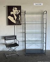 Photo showing black and white Betty Blue artwork, chrome and black director's chair beside chrome and glass shelving unit.