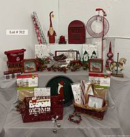 Photo showing the full layout of red Christmas decor items including Santas, metal mailbox, wreath, carousel horse, candles, baskets, plates and gift tins on a table.