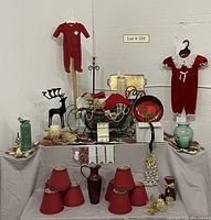 Wide view of all assorted red Christmas and holiday items arranged on display including baby clothes, metal sleigh, red chandelier shades, and mixed decor items.