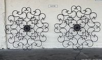 Two large black metal circular wall decor pieces with intricate scrollwork, approximately 36 inches in diameter each, displayed side by side leaning on a white wall.