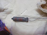 Close-up of one small radio tube with red markings and wire leads, lying on a soft white surface.