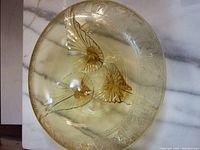 Top-down photo showing the honey-colored depression glass console bowl with butterfly embossing and etched rim details on a marble surface.