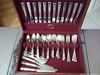 Overall view of open wooden chest containing forks, spoons and knives arranged in red velvet lining
