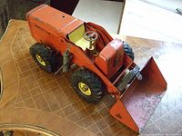 Front and side view of orange Nylint payloader toy showing wear, large tires, steering wheel, and bucket.