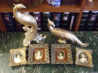 Photo showing 4 cameo prints in ornate gold-tone frames and 2 gold-tone Syroco peacock statues on a green marble surface.