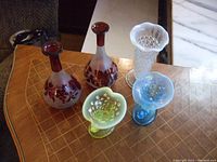 Five antique glass vases: three Fenton cornucopia style in blue, yellow, and white hobnail glass; two etched ruby red glass vases with floral designs and pontil bases.