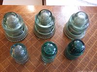 Top and side view of 6 glass telegraph insulators arranged on a surface showing their shape and color.