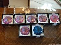 Seven glass diamond paperweights, six pink and one blue, all displayed in their original black and white satin-lined boxes.