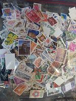 Large plastic bag filled with many small, colorful U.S.A. postage stamps showing various designs and faces, some with cancellation marks.