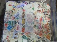 Large clear plastic bag filled with hundreds of loose mixed used stamps from worldwide origins in various colors and designs.