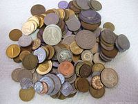 Top view of a large pile of assorted circulated coins from various countries showing different sizes, colors, and symbols including a prominent German eagle coin.