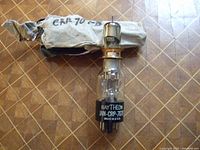 Raytheon JAN-CRP-707B vintage transmitter tube with original paper packaging behind, showing slight wear and tear on paper but tube itself clear and labeled.