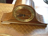 Full view of the mantel clock showing the wooden curved case and brass bezel around the dial.