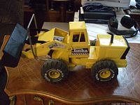 Side view of large vintage yellow Tonka payloader toy on a wooden floor, showing overall shape and condition including the bucket and tires.