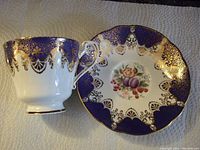 Tea cup and saucer front view showing cobalt blue and gold filigree design with fruit motif on saucer.