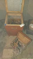 Open wooden storage box on wheels showing metal lining and assorted wooden mallet heads and handles.