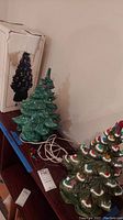 Two unboxed ceramic Christmas trees displayed on shelf with original box behind