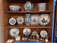 Overview of wooden shelf displaying multiple blue and white Delft ceramic pieces and one multicolored mug