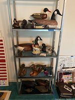 Metal shelving unit displaying approx. 14 wooden decoys and one ceramic duck figurine across four shelves