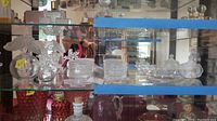 Overall display case shelf showing multiple Lalique glass pieces including atomizers, trinket dishes, and jar behind blue tape