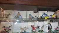 Shelf display of multiple Lenox porcelain bird figurines with styrofoam packing and boxes