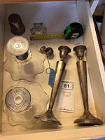 Photo shows two weighted sterling silver candlesticks, glass bowls with weighted bases, a small silver cup, and a tea leaf ball with chain all arranged in a drawer