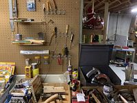 Photo of pegboard with hand tools including hammers, wrenches, brushes, and hardware supplies on shelf and hooks