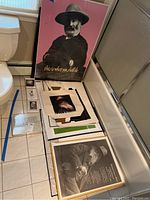 Overall view of two large posters, tote bag and smaller prints arranged on bathroom floor