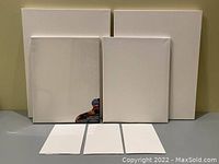 Seven assorted blank canvases in various sizes displayed standing up on a surface.