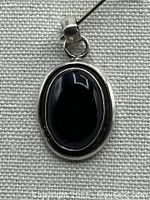 Close-up front view of oval black onyx stone set in handmade silver 925 pendant with loop bail.