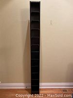 Front view of the tall slim narrow shelving unit against beige wall showing full height and shelf count.