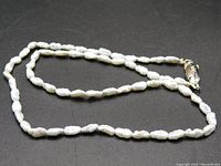 Full necklace laid flat showing the string of irregularly shaped pale dove gray freshwater pearls and silver clasp stamped 'Silver'.