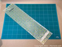 OLFA cutting mat and Omnigrid ruler sealed in plastic displayed together showing grid lines and solid color surface mat.