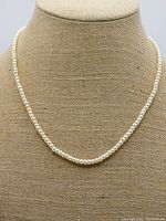 Necklace displayed on a bust showing the uniform string of cream pearls.