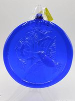 Front view of cobalt blue round sun catcher with embossed hummingbird and flower design, clear stand visible