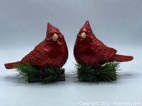 Front view of two red cardinal bird decorations with glittered wings perched on pine bases.