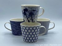 Four Royal Doulton Pacific Blue porcelain mugs arranged with one stacked on top, showing distinct blue and white patterns and handles.