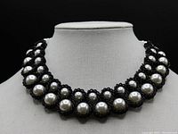 Front view of the pearl and black chain bib necklace displayed on a bust stand showing two sizes of pearls and black chain wrapping.