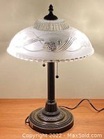 Full view of Victorian style table lamp on wooden surface, lit to show etched floral glass shade and metal base.