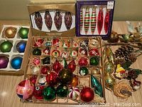 Full view of assortment including ornaments in cardboard boxes, decorative birds, pine cones, and icicle ornaments.