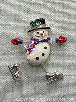 Front view of the snowman brooch showing colorful enamel details, coiled wire arms and legs, and silver-tone ice skates.