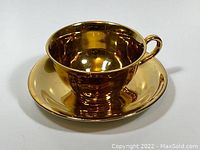 Gold metallic tea cup and matching saucer displayed together showing reflective finish and shape.