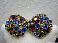Pair of vintage multi-colored rhinestone clip-on earrings showing front view with clustered round faceted rhinestones in jewel tones of purple, blue, green and clear on gold-tone setting.