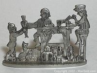 Front view of pewter Christmas elves figurine showing elf holding nutcracker, another working at sewing machine, and a third elf sitting and painting.